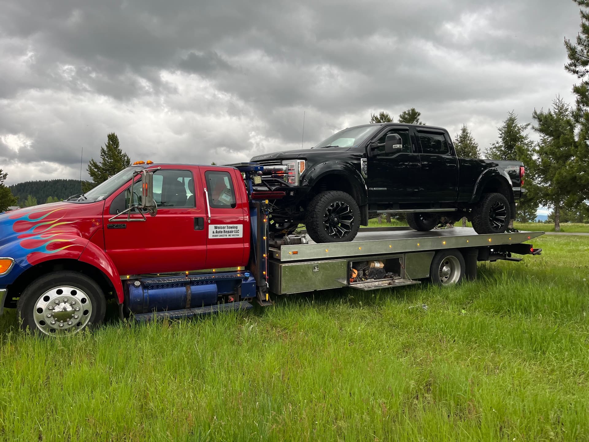 Weiser Towing red flatbed carrying a black Ford pickup in an Idaho field